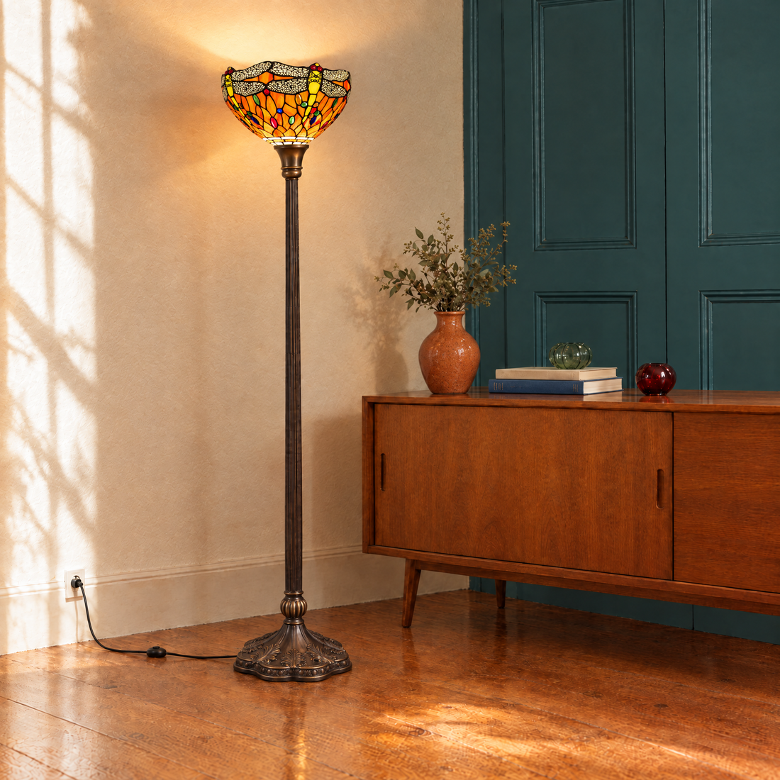 Tiffany Stehlampe Libellula Tramonto als Uplighter neben Holzkommode und grüner Tür im Wohnzimmer