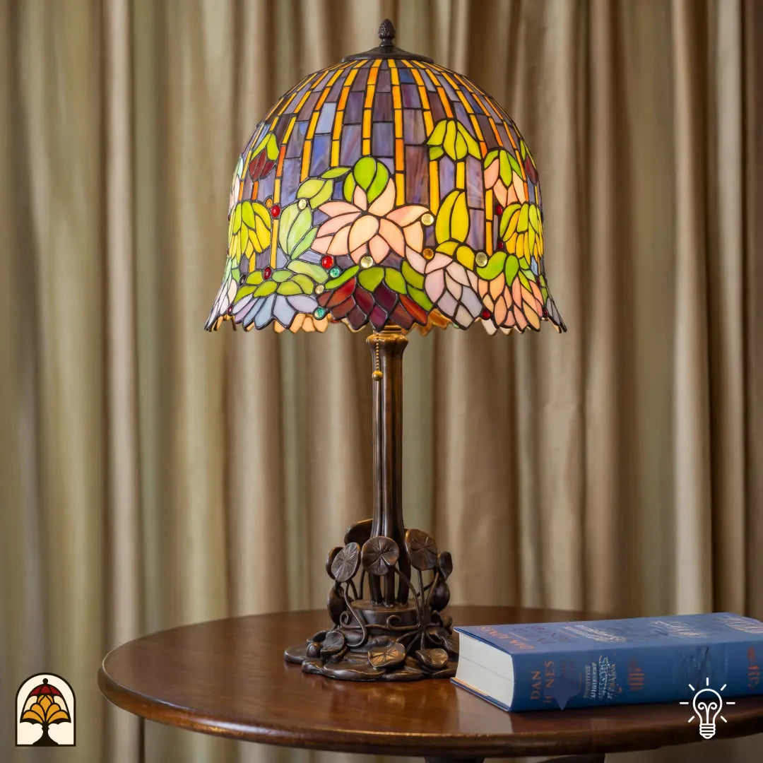 Tiffany tafellamp Pond Lilia in sfeervol interieur op ronde bijzettafel – waterlelie glas-in-lood kap verlicht, bronzen voet met bladmotief