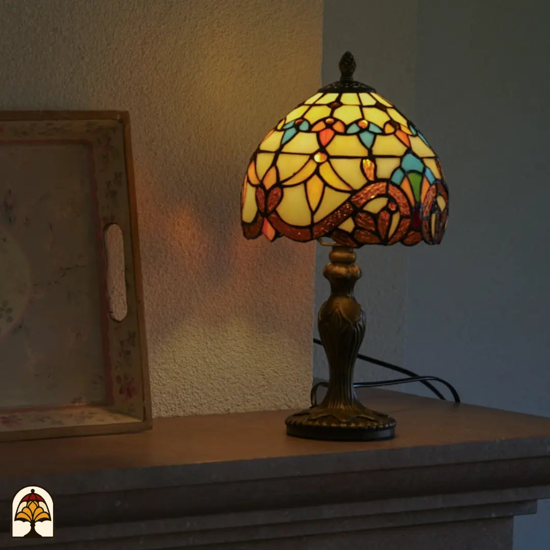 Verlichte Tiffany tafellamp Baroque op schoorsteenmantel naast schilderij in lijst – warme amber en gele gloed door barokke koepelkap