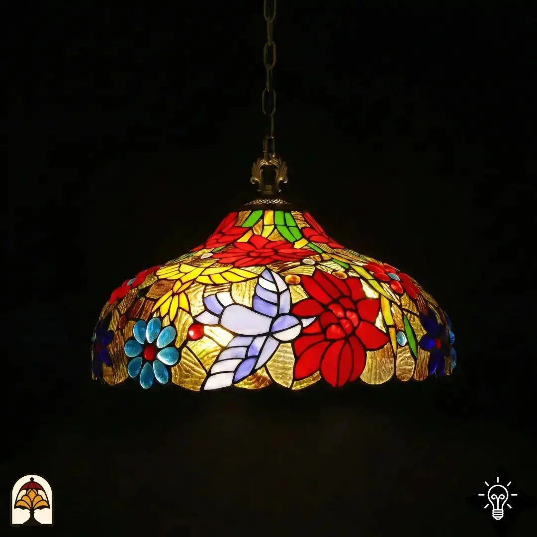 Tiffany lamp hanglamp verlicht in donkere omgeving, koepelvorm met rode poinsettia-bloemen, blauwe madeliefjes, wit-lavendel vlinder en gele bladpanelen op goudkleurig glas, opgehangen aan bronzen ketting met bronzen fitting