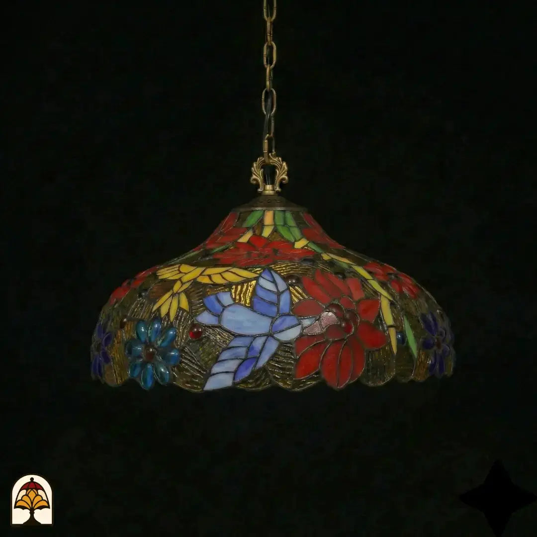 Tiffany lamp hanglamp onverlicht in donkere omgeving, koepelvorm met rode poinsettia-bloemen, blauwe madeliefjes, wit-lavendel vlinder en gele bladpanelen, bronzen gekartelde onderkant, opgehangen aan bronzen ketting
