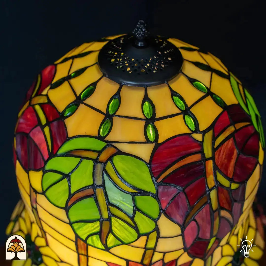 Close-up bovenkant Tiffany kap — geperforeerd ventilatierooster, gele/amber glas met groene bladvormige elementen rondom