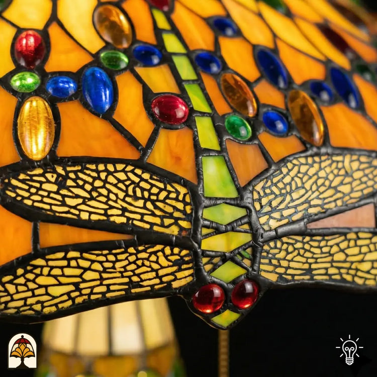 Detailopname van tiffany lamp libelle-rand onderaan de kap verlicht, geel-goudkleurige libellen met geaderde vleugels in glas-in-lood, blauwe en bruine ovale glaskralen en rode ronde kralen