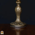 Close-up bronzen Art Nouveau voet tafellamp Libellula Azul ⌀20 op houten tafelblad, donkere achtergrond, fijn bladrelief op steel en voetplaat