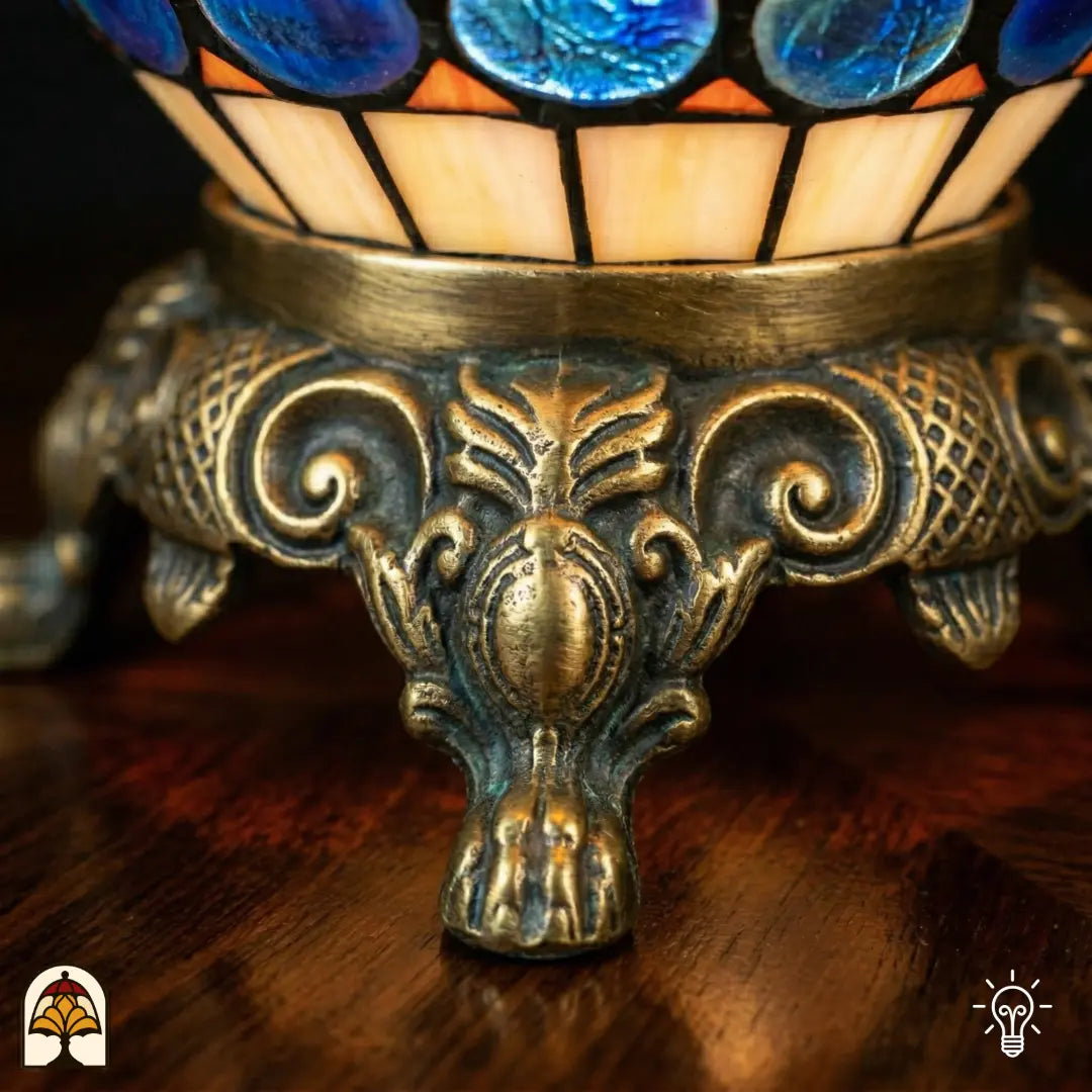 Detailopname van tiffany lamp bronzen siervoet met leeuwenpoten en acanthusblad-ornament, crème en oranje glas-in-lood en blauwe glaskralen bovenaan zichtbaar
