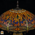 Detailopname van tiffany lamp kapbovenzone onverlicht, amberkleurig glas met blauwe, groene en bruine ovale glaskralen in banden, trekkettingen en bronzen ventilatieplaat zichtbaar