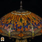 Detailopname van tiffany lamp kapbovenzone onverlicht, amberkleurig glas met blauwe, groene en bruine ovale glaskralen in banden, trekkettingen en bronzen ventilatieplaat zichtbaar