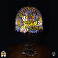 Verlichte Tiffany tafellamp Pond Lilia met koepelvormige kap, blauwe en gele verticale strepen in glas-in-lood, witte waterlelies, groene bladeren en gekleurde ronde accenten, bronzen Art Nouveau waterlelieblad-voet, donkere achtergrond