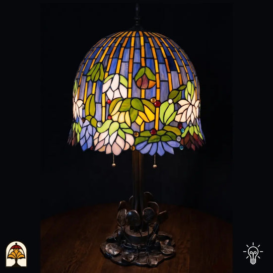 Verlichte Tiffany tafellamp Pond Lilia met koepelvormige kap, blauwe en gele verticale strepen in glas-in-lood, witte waterlelies, groene bladeren en gekleurde ronde accenten, bronzen Art Nouveau waterlelieblad-voet, donkere achtergrond