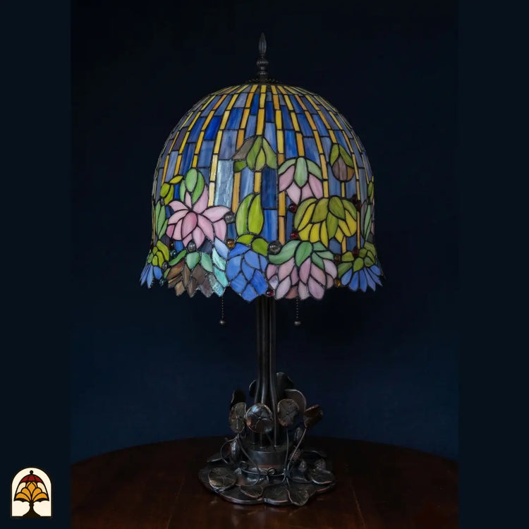 Onverlichte Tiffany tafellamp Pond Lilia op donkerblauwe achtergrond, koepelkap met blauwe strepen, roze waterlelies en groene bladeren, Art Nouveau waterlelieblad-voet