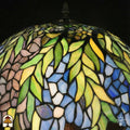 Close-up bovenkant verlichte Tiffany kap — groene bladeren, blauw/paarse en gele glasvlakken