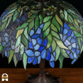 Close-up onverlichte Tiffany kap — groene bladeren, blauwe en paarse bloemen in wisteria-stijl