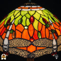 Close-up verlichte kap Libellula Azul ⌀30, oranje glas-in-lood panelen met geel-groene bladmotieven, rode en groene ovale juwelen en libellenfries onderaan