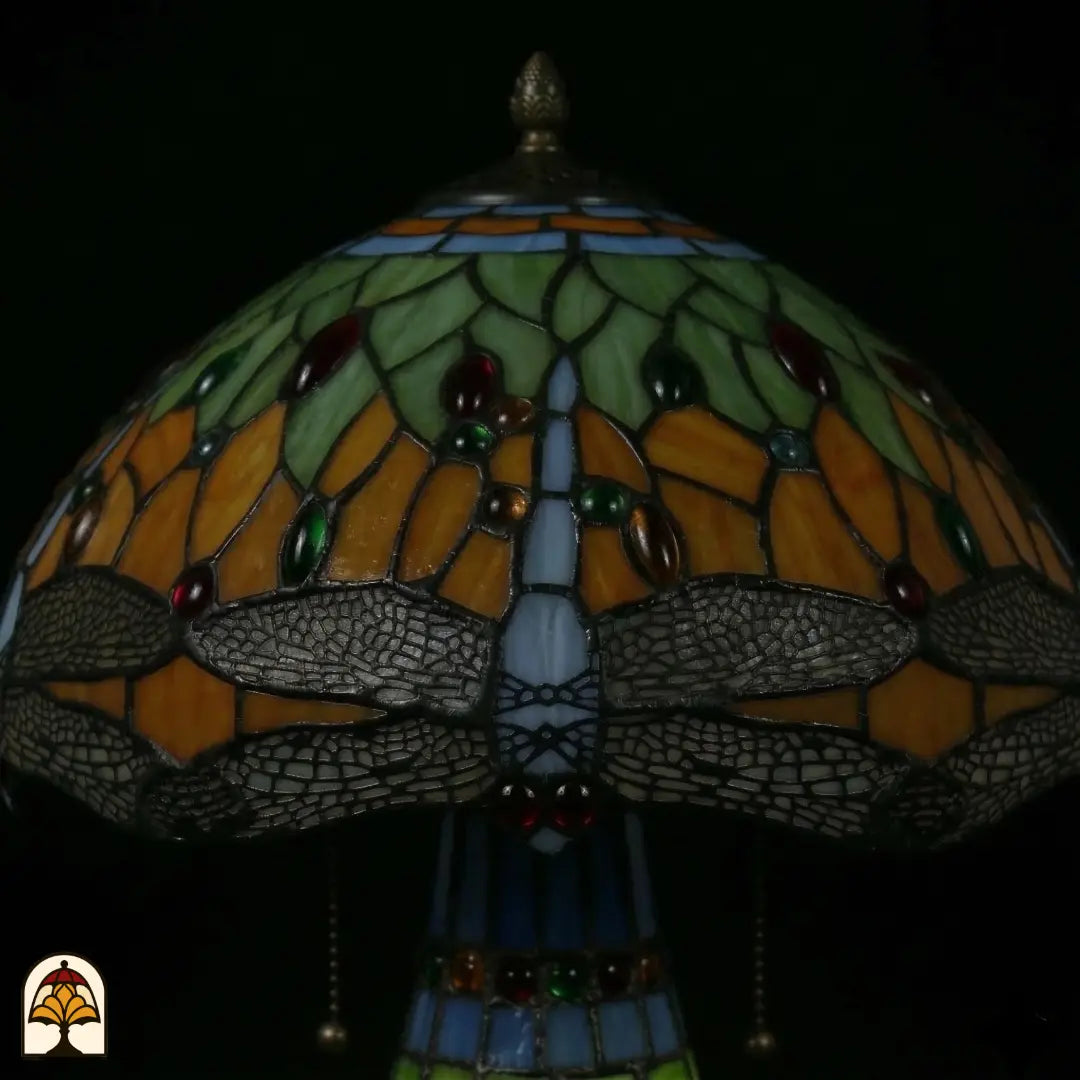 Close-up onverlichte kap Libellula Lumina ⌀30, groene en oranje glas-in-lood panelen met rode, groene en amber juwelen, blauwe libellenfries langs rand
