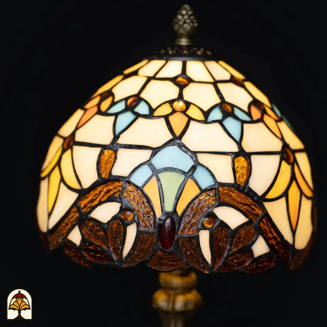 Close-up verlichte koepelkap Tiffany tafellamp Baroque – crème en amber glas met lichtblauwe en turquoise boogvormen, rode edelsteen in center