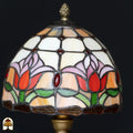 Close-up onverlichte koepelkap Tiffany tafellamp Tulipa – roze en rode tulpen op crème en oranje glas, rode edelsteen in center