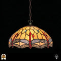 Verlichte Tiffany hanglamp Libelle, koepelvormige geel-amber kap met rode druppelvormige accenten, blauwe details en libellenmotieven in glas-in-lood, donkere achtergrond