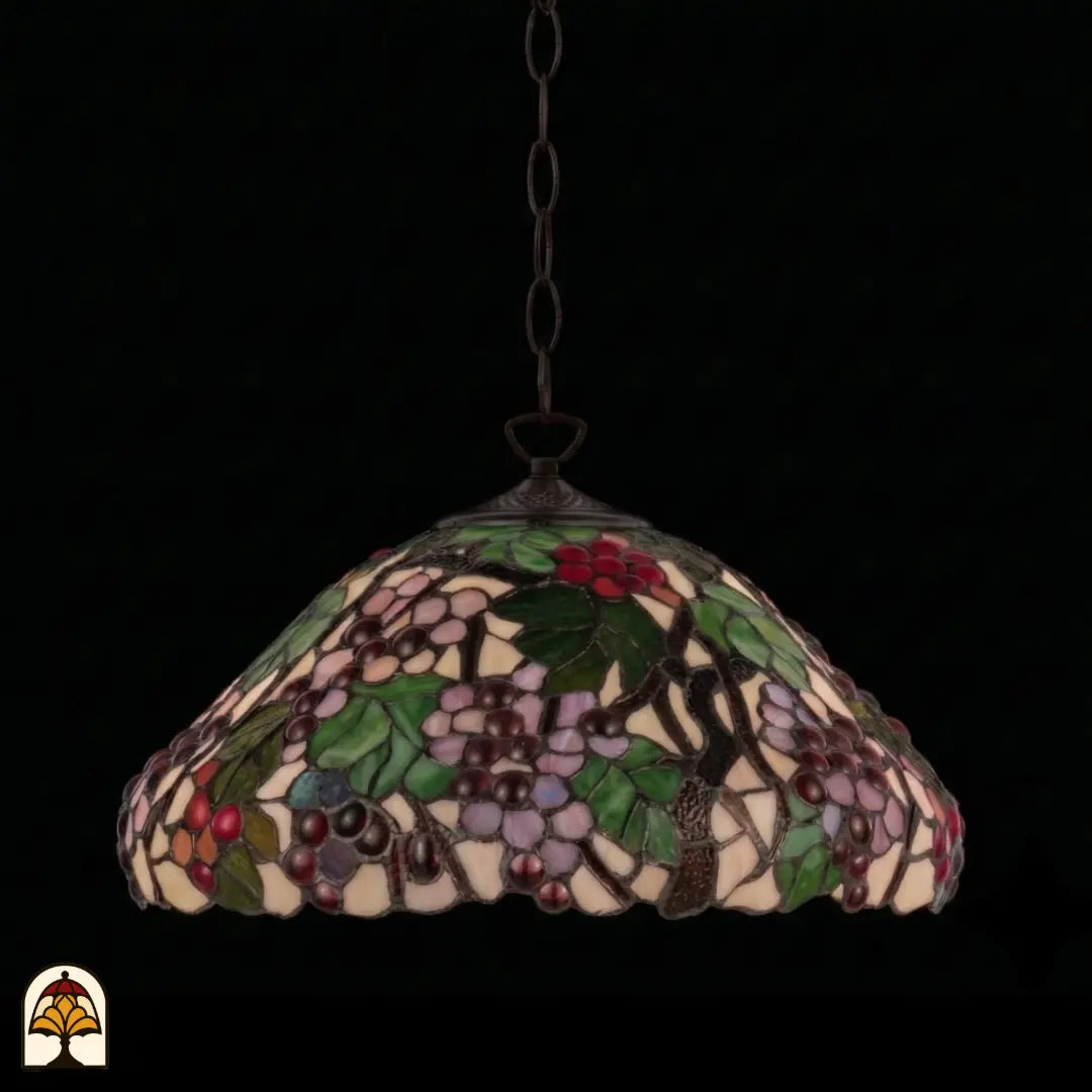Onverlichte Tiffany hanglamp Sylva Berria aan bronzen ketting, koepelvormige kap met lila en rode druiven en groene bladeren, donkere achtergrond