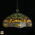 Onverlichte Tiffany hanglamp Libellula Aurelia ⌀50 op donkere achtergrond, kap met gele en groene panelen, grijze libellenfries met rode juwelen langs rand, bronzen ketting