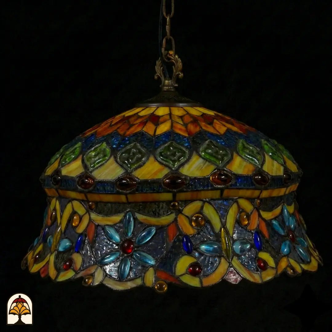 Tiffany lamp hanglamp onverlicht van dichterbij, koepelvormige kap met ambergele bovenzone met groene glaskralen, en blauwe onderzone met lichtblauwe bloemkralen en rode glaskralen op paarsgrijs glas