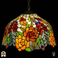 Tiffany lamp hanglamp verlicht van dichterbij, koepelvormige kap met oranje rozen, rode ovale glaskralen, gele rozen en groene bladeren op witte getextureerde achtergrond, opgehangen aan bronzen ketting