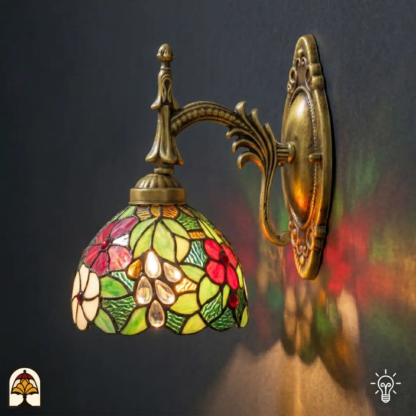 Verlichte Tiffany wandlamp Floral Garden op gebogen bronzen arm, kap met rode en roze bloemen, groene bladeren en gele accenten in glas-in-lood
