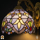 Close-up verlichte kap Tiffany wandlamp Royal Mosaic – lavendelblauwe en crèmegele glas-in-lood vlakken met oranje, rode en paarse juwelen