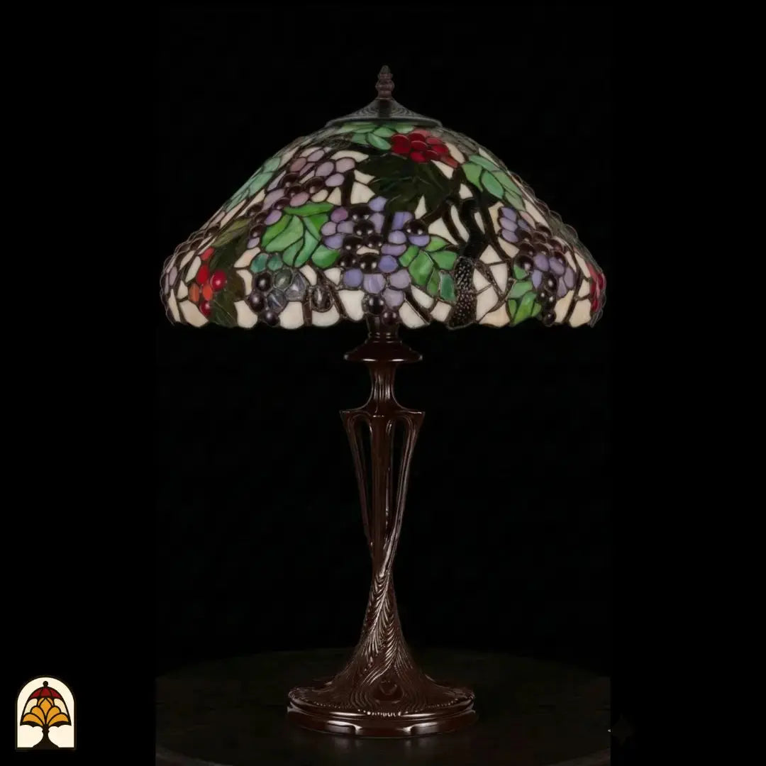 Onverlichte Tiffany tafellamp Sylva Berria op donkere achtergrond, kap met lila en rode druiventrosjes en groene bladeren, slanke bronzen Art Nouveau vaasvoet