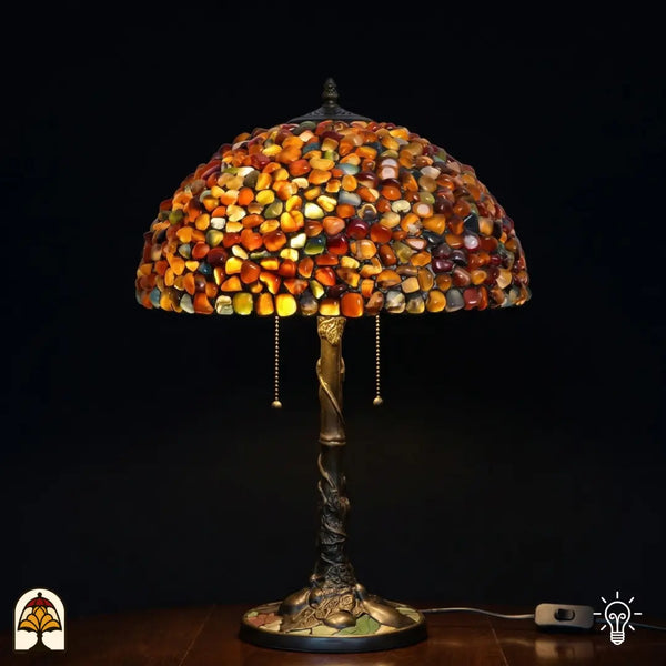 Verlichte Tiffany tafellamp Stone Mosaic Amber ⌀40 cm op donkere achtergrond – koepelkap van amber, oranje en okerkleurige gepolijste stenen, bronzen boomstamvoet met twee trekschakelaars