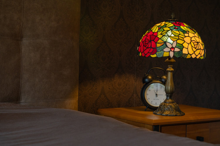 Handgemaakte Tiffany tafellamp met rood-groen bloemenpatroon van echt glas-in-lood, geplaatst op een klassieke bronzen voet voor een sfeervol interieur.