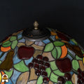 Close-up bovenkant kap Tiffany tafellamp Frutta Viva — geperforeerd ventilatierooster, fruitmotief met rode appels en druiven rondom, groene bladeren