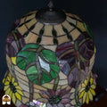 Close-up Tiffany kap onverlicht — bovenkant kap, amber/geel glas met groene decoratieve elementen, paarse en rode bloemen