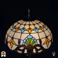 Close-up kap Tiffany vloerlamp Barok andere hoek — crème bovenzijde met blauwe en oranje tulpvormen, groene waaierpatroon onderaan, bronzen decoratieve rand