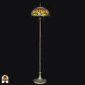 Tiffany vloerlamp Libellula Aurea onverlicht op zwarte achtergrond — amber/geel/bruine kap met libellenrand, lange paal met brede voet