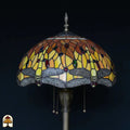 Close-up kap Tiffany vloerlamp Libellula Aurea onverlicht — geel/oranje/amber glas met rode, blauwe en groene edelstenen, grijze libellenrand onderaan