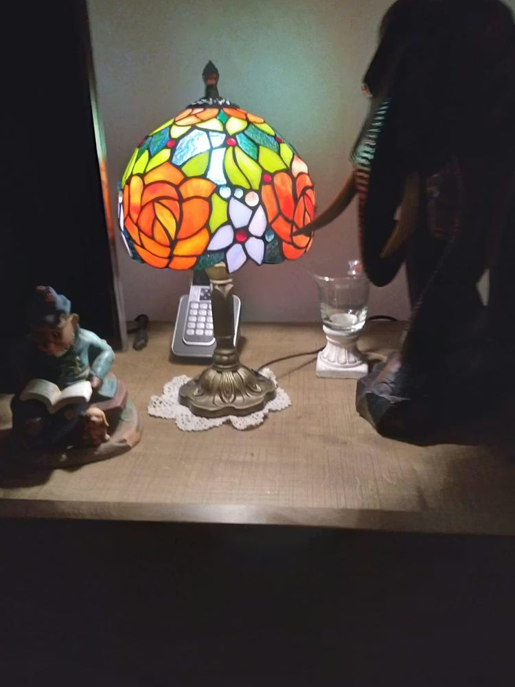 Tiffany tafellamp met oranje rozen en paarse bloemen in glas-in-lood kap, warm en sfeervol licht voor een klassiek interieur.
