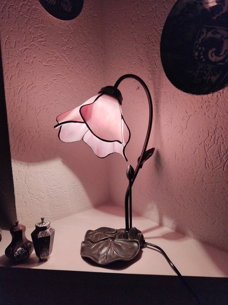 Tiffany tafellamp met roze bloemvormige kap en metalen bladvoet, warm sfeervol licht voor een vintage interieur.