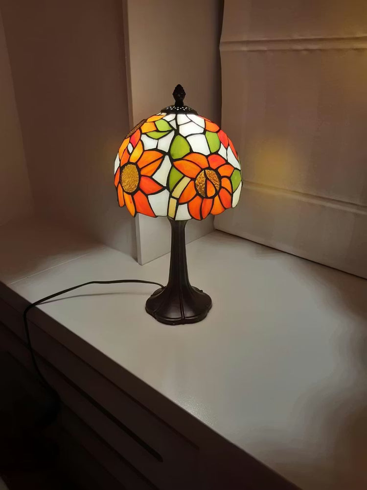 Tiffany tafellamp met oranje glazen zonnebloemen en sierlijke metalen voet, warm en decoratief sfeerlicht voor een klassiek interieur.