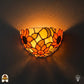 Tiffany wandlamp Solea Girasole verlicht op muur – halfronde kap met zonnebloemen in oranje en geel glas